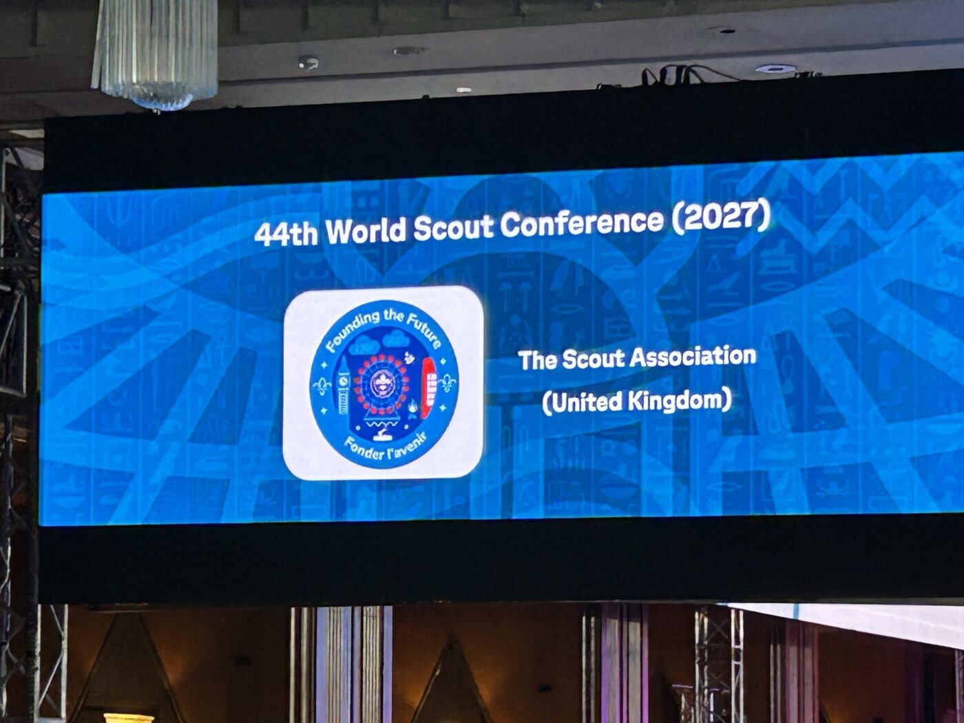 A slide is displayed on a conference screen announcing the hosts of the next World Scout Conference