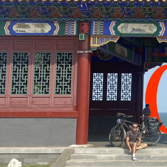 A scout leader sits outside an Asian temple, with his bicycle